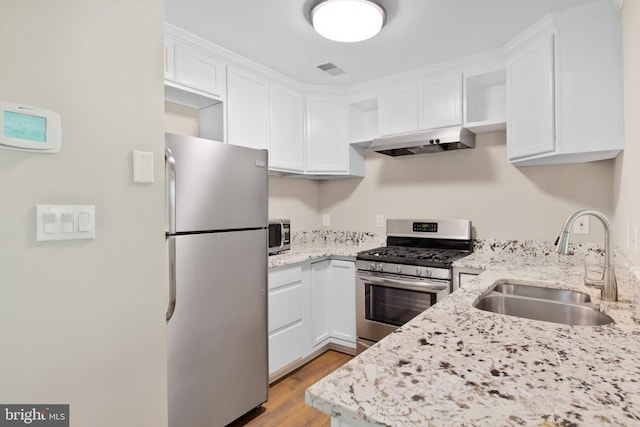 kitchen featuring white cabinets, light stone countertops, a sink, stainless steel appliances, and under cabinet range hood