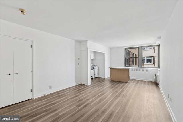 unfurnished living room with baseboards, radiator heating unit, and wood finished floors