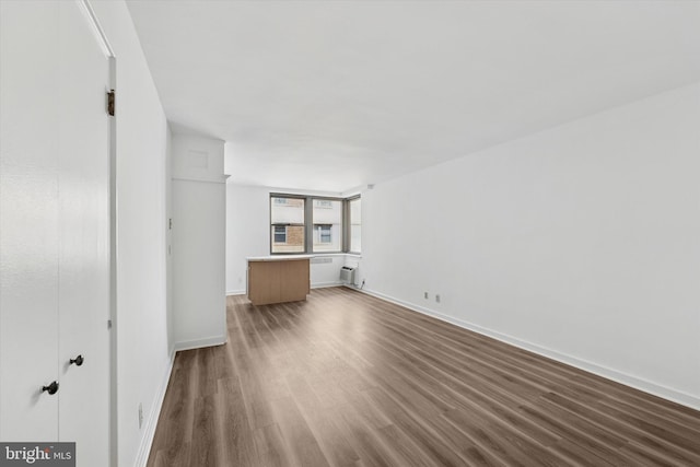 unfurnished living room with baseboards and dark wood-type flooring