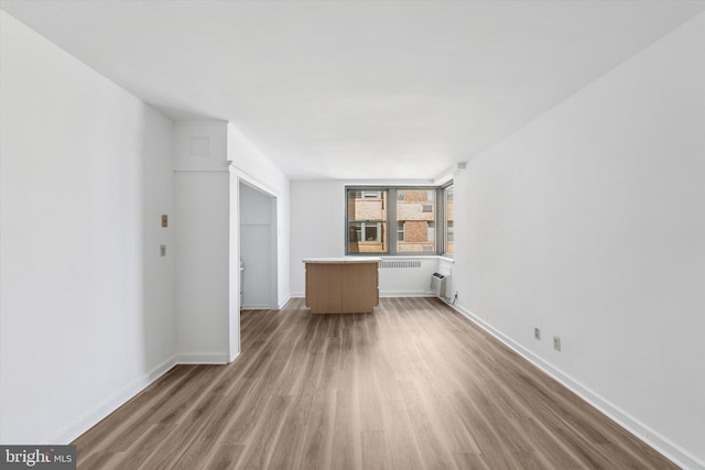 unfurnished living room featuring baseboards, a wall unit AC, and wood finished floors