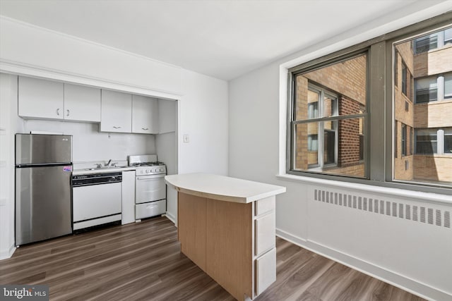 kitchen with a sink, white appliances, light countertops, radiator, and dark wood-style floors