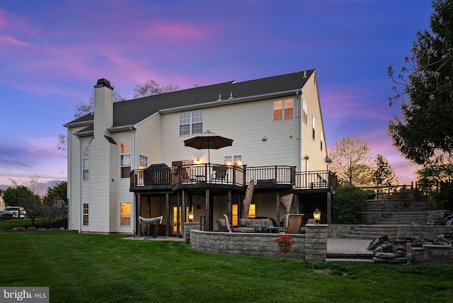 back of house at dusk with a lawn, a chimney, a deck, and a patio