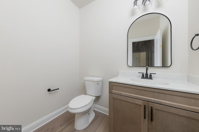 half bathroom featuring baseboards, toilet, vanity, and wood finished floors