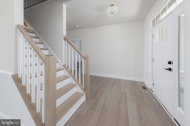 foyer with wood finished floors, visible vents, baseboards, and stairway