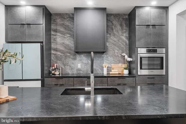 kitchen featuring stainless steel oven, gray cabinets, a sink, and freestanding refrigerator