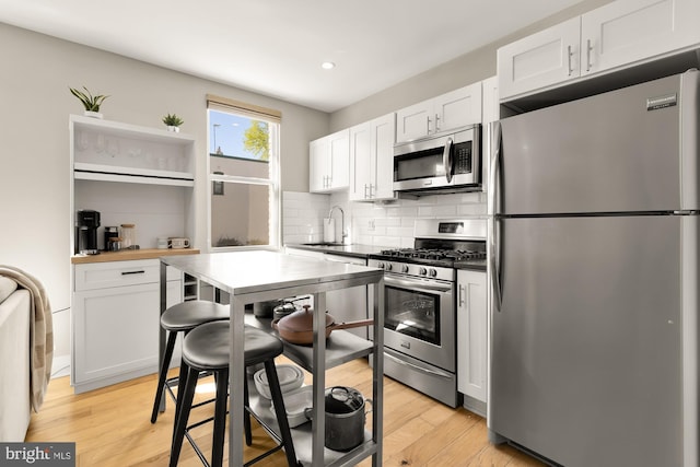 kitchen featuring a sink, light wood-type flooring, appliances with stainless steel finishes, decorative backsplash, and recessed lighting