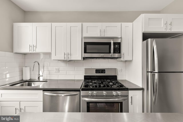 kitchen with a sink, stainless steel appliances, white cabinetry, and dark countertops