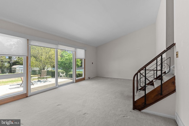 unfurnished living room featuring baseboards, carpet floors, and stairway