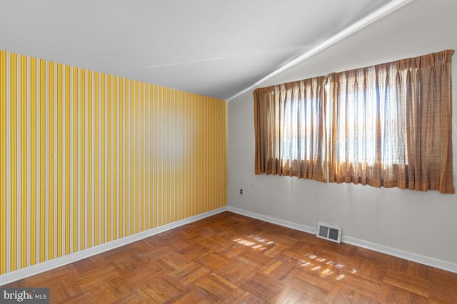empty room featuring visible vents, vaulted ceiling, and baseboards