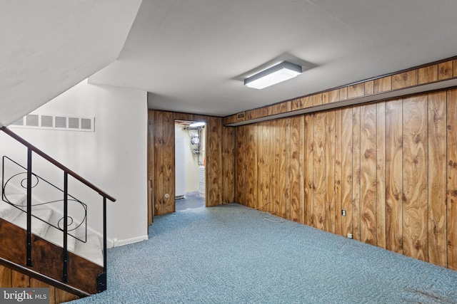finished basement featuring baseboards, visible vents, carpet, stairway, and wooden walls