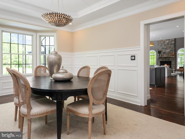 dining space with crown molding, a decorative wall, dark wood finished floors, and a stone fireplace