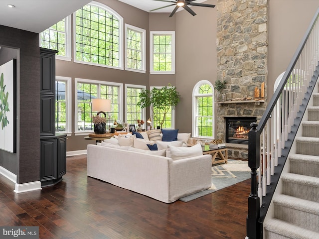 living room with a fireplace, stairs, a ceiling fan, baseboards, and dark wood-type flooring