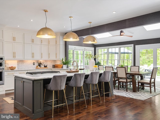 kitchen featuring gas cooktop, tasteful backsplash, white cabinetry, and an island with sink