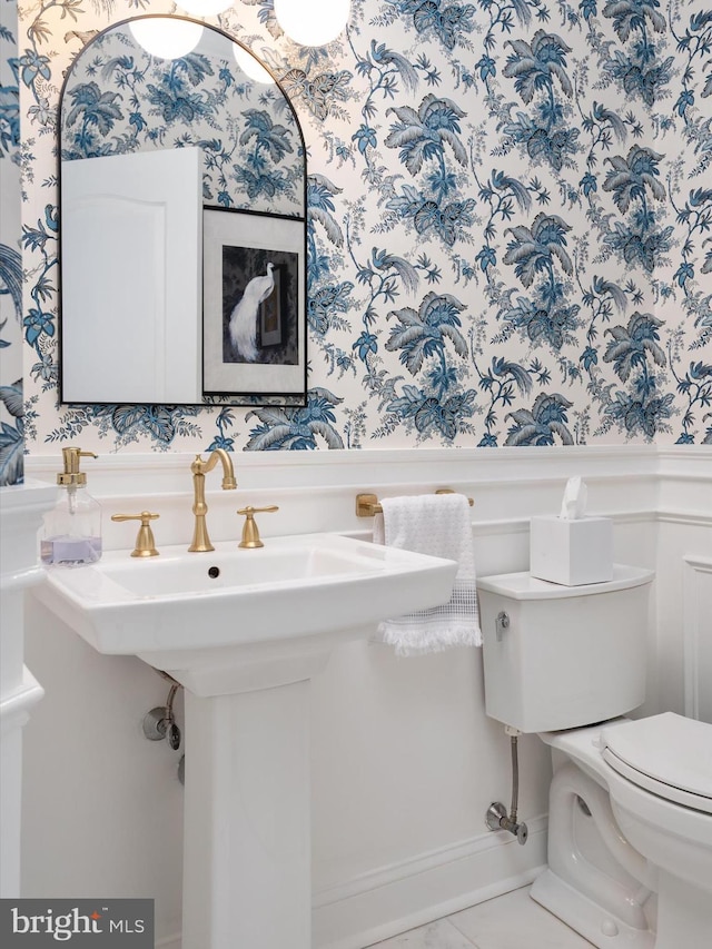 half bathroom featuring wainscoting, toilet, and wallpapered walls