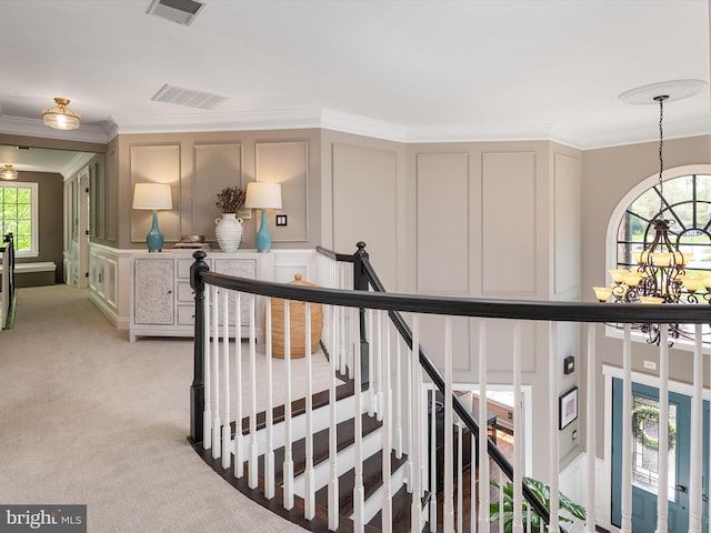 hallway featuring visible vents, ornamental molding, an upstairs landing, and a decorative wall