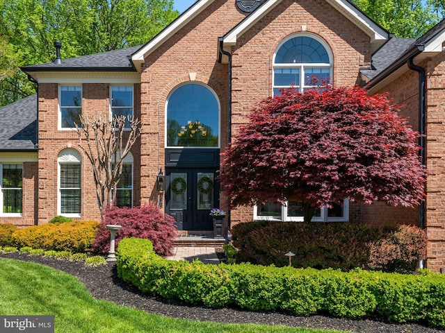 traditional-style house featuring brick siding, roof with shingles, and french doors