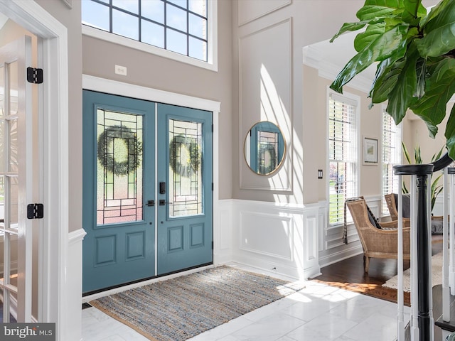 foyer entrance with a healthy amount of sunlight, a wainscoted wall, french doors, and marble finish floor