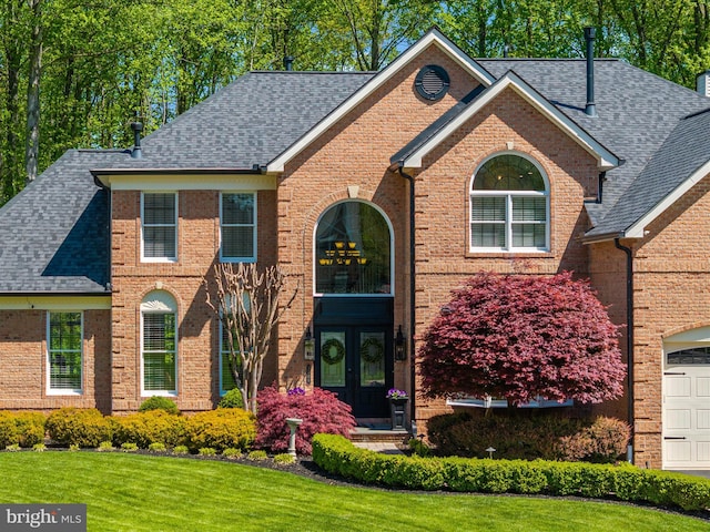 view of front of house with a shingled roof, a front lawn, brick siding, a garage, and french doors