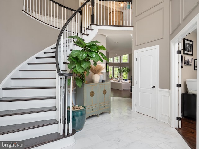 entryway featuring marble finish floor, a towering ceiling, and stairway