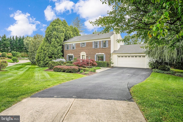 colonial inspired home with a garage, brick siding, a front lawn, and aphalt driveway