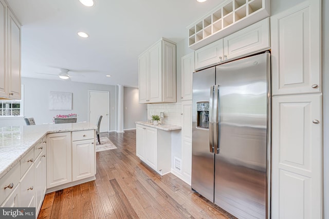 kitchen featuring light stone countertops, light wood-type flooring, recessed lighting, stainless steel fridge with ice dispenser, and backsplash