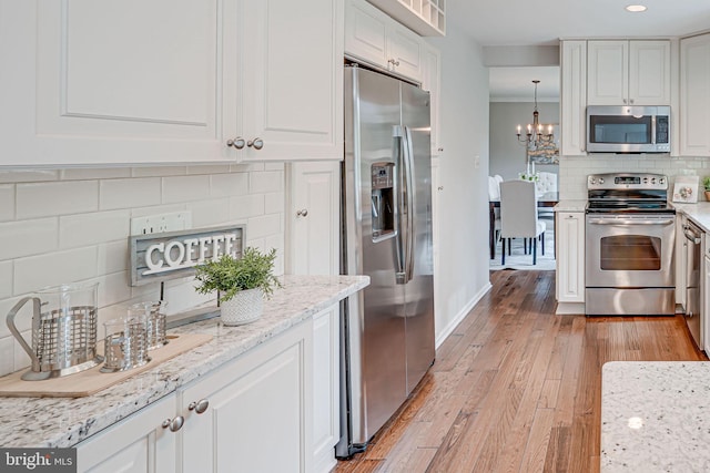 kitchen featuring tasteful backsplash, white cabinets, a notable chandelier, light wood-style floors, and stainless steel appliances