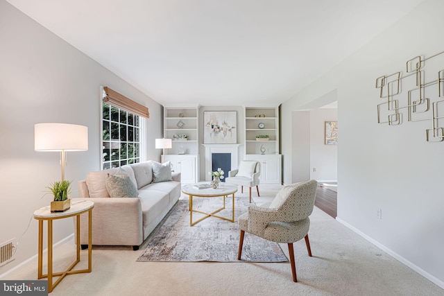living area featuring baseboards, a fireplace, built in shelves, and visible vents
