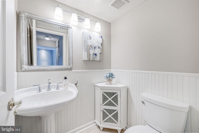 bathroom featuring visible vents, tile patterned flooring, wainscoting, toilet, and a sink