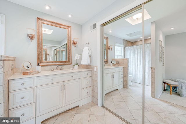 full bathroom featuring a sink, a skylight, walk in shower, and two vanities
