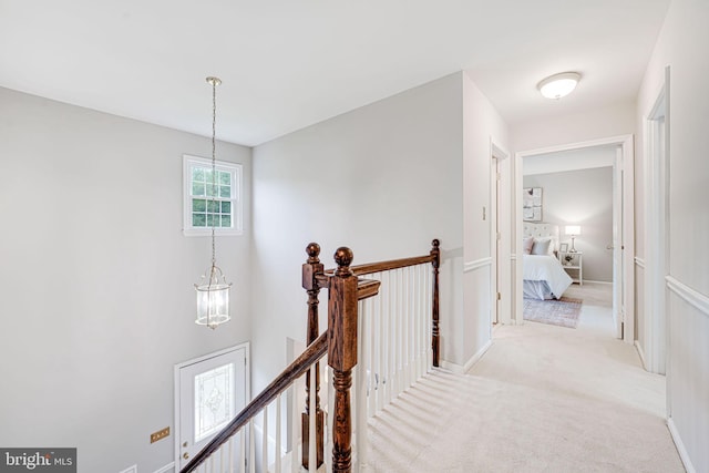 hall featuring a chandelier, light carpet, and an upstairs landing