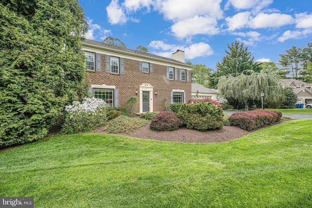 colonial-style house featuring brick siding, a chimney, and a front lawn