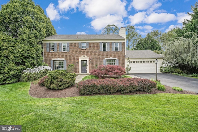 colonial-style house with a garage, a front lawn, aphalt driveway, a chimney, and brick siding