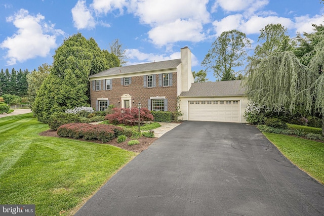 colonial house featuring an attached garage, a front lawn, brick siding, aphalt driveway, and a chimney