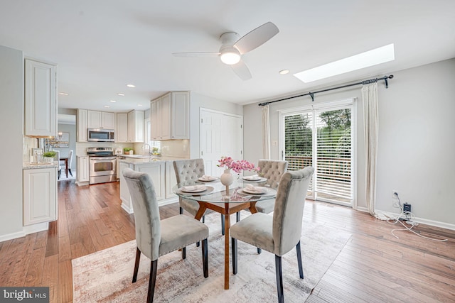 dining space featuring light wood-style floors, baseboards, ceiling fan, and a skylight