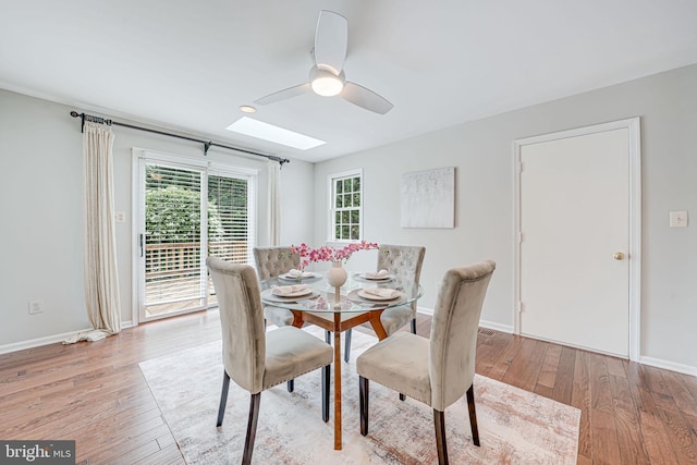 dining area with light wood-type flooring, baseboards, ceiling fan, and a skylight
