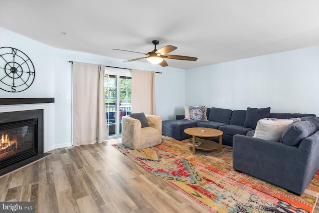 living room featuring a ceiling fan, a glass covered fireplace, and wood finished floors