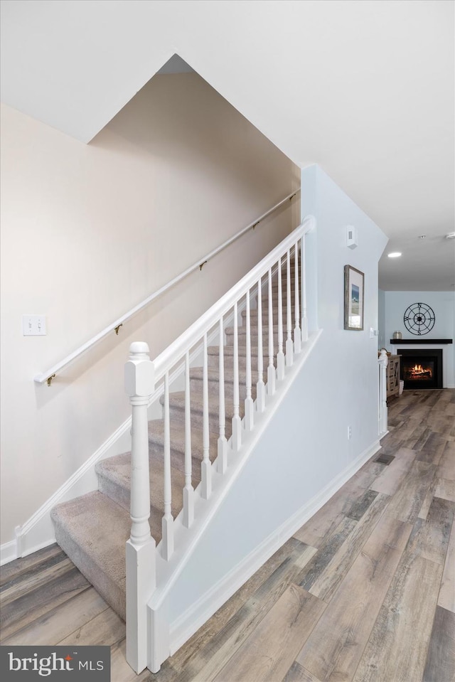 stairway featuring baseboards, a lit fireplace, and wood finished floors