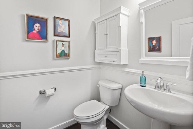 half bath with toilet, baseboards, and a sink