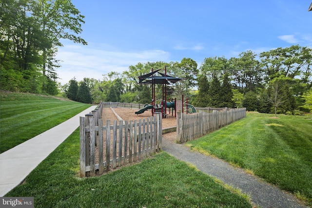 view of community featuring a lawn, fence, and playground community