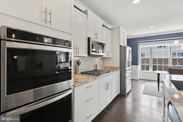 kitchen featuring dark wood-type flooring, white cabinetry, light stone counters, backsplash, and stainless steel appliances