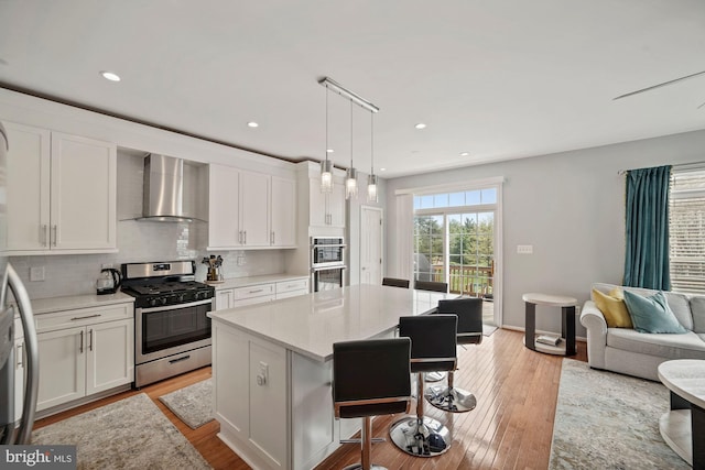 kitchen with white cabinetry, appliances with stainless steel finishes, wall chimney range hood, light countertops, and a breakfast bar area