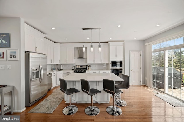 kitchen with light countertops, wall chimney range hood, white cabinetry, and stainless steel appliances