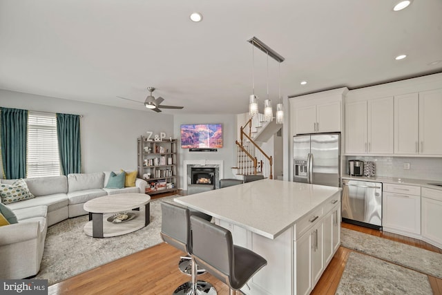 kitchen featuring white cabinets, light countertops, light wood-style flooring, appliances with stainless steel finishes, and open floor plan