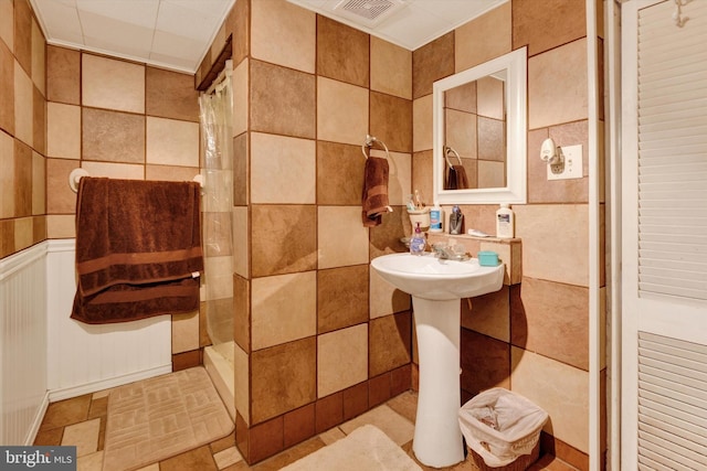 bathroom featuring a tile shower, tile walls, and visible vents