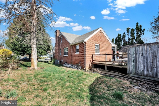 view of home's exterior featuring a lawn, a chimney, central air condition unit, a deck, and brick siding