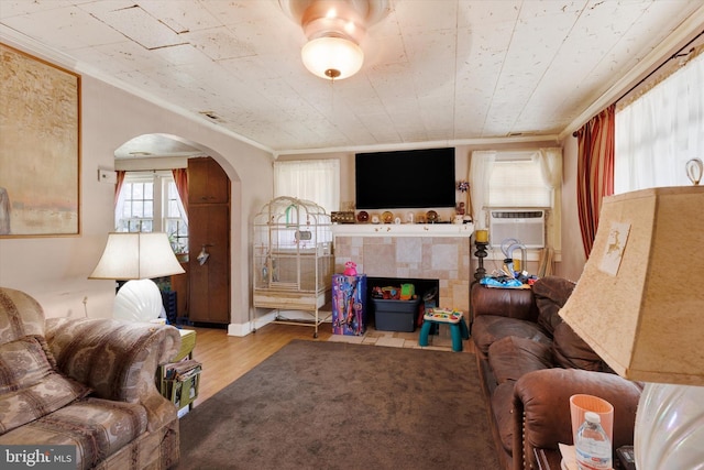 living area featuring arched walkways, wood finished floors, a tile fireplace, and crown molding