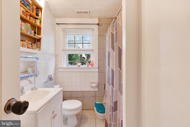 full bathroom featuring tile patterned floors, visible vents, toilet, vanity, and tile walls