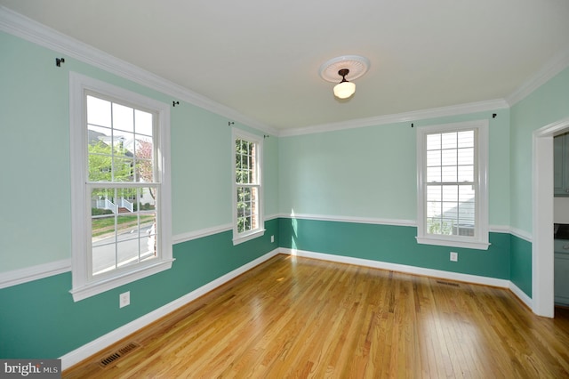 empty room with wood finished floors, visible vents, crown molding, and baseboards