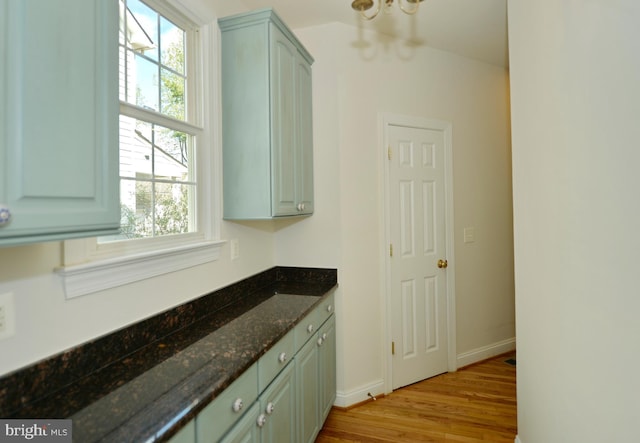 interior space featuring light wood-style floors, baseboards, dark stone counters, and an inviting chandelier