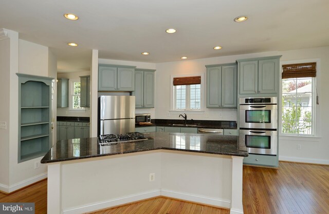 kitchen featuring stainless steel appliances, a sink, dark stone counters, plenty of natural light, and light wood-style floors